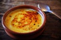Typical `crema catalana` served on a clay plate on a rustic wooden table with a spoon.