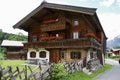 Typical dark wooden Tyrolean house with balcony with red flowers and mountains behind.