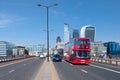 Typical double decker buses on the London Bridge with a view of the City