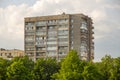 Typical facade of an old brick nine-story building in the post-Soviet countries on a background of green trees