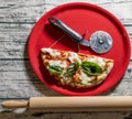 Typical Italian pizza cut in half with the special wheel in a red plate with a wooden rolling pin next to it