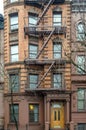 Typical New York City Apartment Building with Fire Escape Ladders and Yellow Wooden Door at the Entrance