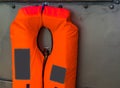 Typical orange life jacket hanging on a metal wall, water transport safety, marine background