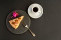A typical Portuguese cake made of cookies on a black slate with a fork, espresso and a flower on a black background