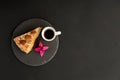 A typical Portuguese cake made of cookies called Bolo de Bolasa on a black slate with espresso and a flower on a black background.