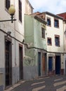 a typical quiet empty street in funchal madeira with old traditional houses painted in faded pastel peeling paint and a cobbled