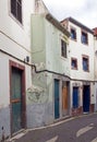a typical quiet empty street in funchal madeira with old traditional houses painted in faded pastel peeling paint and a cobbled