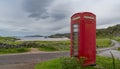 Typical red English phone booth in the middle of nowhere next to a picturesque beach in Scotland with a coastal road Royalty Free Stock Photo