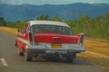 An old classic yank tank car on Cuban country side with a view of the road, mountain and forest, Cuba