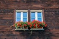 Typical window of wooden Alpine chalet. Wooden hut, red flowers in window. Traditional Alpine architecture. Alps. Alpine hut. Royalty Free Stock Photo