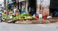Typically Asian street corner vegetable market with selection of fruits and vegetables in path in front grimy building
