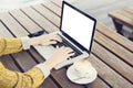 Typing girl with blank laptop screen, smartphone and cup of coffee on wooden table outdoor, mock up Royalty Free Stock Photo