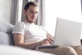 Typing new blog post. Handsome young man using his laptop with smile while sitting on the couch at home. Royalty Free Stock Photo