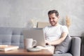 Typing new blog post. Handsome young man using his laptop with smile while sitting on the couch at home. Royalty Free Stock Photo