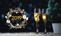 2019 Typography Art. Two Glasses of Champagne and Small Christmas Tree Dark Glow Lights Background