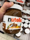 View on isolated Nutella glass jar hold by hand in front of shelf