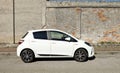 White Toyota Yaris hybrid at the road side. Side view, grunge concrete wall with exposed bricks on background.