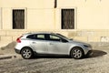 Silver colored Volvo V40 at the roadside of a cobblestone road with an old building on behind.