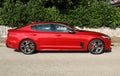 New red Kia Stinger GT at the roadside. Side view. Royalty Free Stock Photo