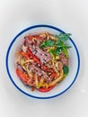 Udon noodles with meat in a plate on a white surface. With vegetables greens