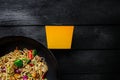 Udon stir fry noodles with chicken and vegetables in wok pan on black wooden background. With a box for noodles. Royalty Free Stock Photo