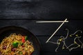 Udon stir fry noodles with chicken and vegetables in wok pan on black wooden background. With chopsticks Royalty Free Stock Photo