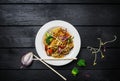 Udon stir fry noodles with meat or chicken and vegetables in a white plate with chopsticks.