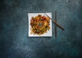 Udon stir fry noodles with meat or duck, vegetables and sesame seeds on a square white plate. With chopsticks. Royalty Free Stock Photo