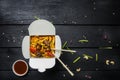 Udon stir fry noodles with meat and vegetables in a box on black background. With chopsticks and sauce. Royalty Free Stock Photo