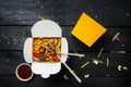 Udon stir fry noodles with meat and vegetables in a box on black background. With chopsticks and sauce. Royalty Free Stock Photo