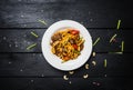 Udon stir fry noodles with meat and vegetables in a white plate on black wooden background. With chopsticks and sauce Royalty Free Stock Photo