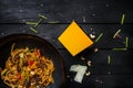 Udon stir fry noodles with meat and vegetables in wok pan on black wooden background. With a box for noodles Royalty Free Stock Photo