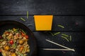 Udon stir fry noodles with seafood and vegetables in wok pan on black wooden background. With a box for noodles Royalty Free Stock Photo