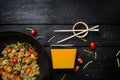 Udon stir fry noodles with seafood and vegetables in wok pan on black wooden background. With a box for noodles Royalty Free Stock Photo