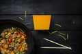 Udon stir fry noodles with seafood and vegetables in wok pan on black wooden background. With a box for noodles Royalty Free Stock Photo