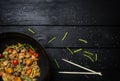 Udon stir fry noodles with seafood and vegetables in wok pan on black wooden background. With a box for noodles Royalty Free Stock Photo