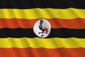 Uganda flag with big folds waving close up under the studio light indoors. The official symbols and colors in banner