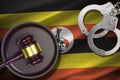 Uganda flag with judge mallet and handcuffs in dark room. Concept of criminal and punishment, background for judgement