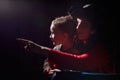 Ugle oman in red sweater and pirate hat with curly hair posing with small boy on black background. Actress mother and actor son in