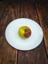 Ugly damaged yellow apple on a white plate on the table