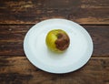 Ugly damaged yellow apple on a white plate
