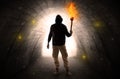 Man walking with burning flambeau in a dark tunnel