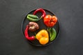 Ugly organic colorful tomato, pepper, cucumber in plate on black concrete. Concept organic vegetables