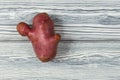 Ugly pink potato on light wooden textured background. Close-up, selective focus. Concept - unusual vegetables and fruits. Reduce