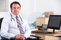 Uk doctor smiling at camera sitting at his desk Royalty Free Stock Photo