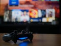 UK, Jan 2020: Sony dualshock 4 controller remote for Playstation 4 with TV screen behind in dark Royalty Free Stock Photo