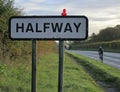 Uk village road sign half way between London and Bristol on the Roman road with a cyclist passing by