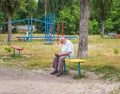 Ukraine. Kyiv - 4 July 2020. An elderly man reads a book in the playground. Children play in the background