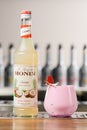 UKRAINE, KYIV - MARCH 12, 2021: bottle of Monin coconut syrup and glass of beautiful thick pink cocktail garnished with