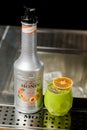 UKRAINE, KYIV - MARCH 12, 2021: bottle of Monin peach syrup and glass of green cocktail with chia seeds and orange slice